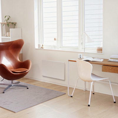 Radiatore elettrico norvegese Klimago™ NOBO TOP bianco installato a parete in un moderno soggiorno luminoso