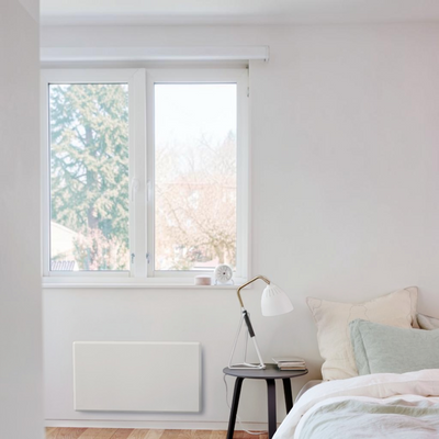 Radiatore elettrico norvegese Klimago™ NOBO TOP bianco a parete installato in una camera da letto moderna e luminosa